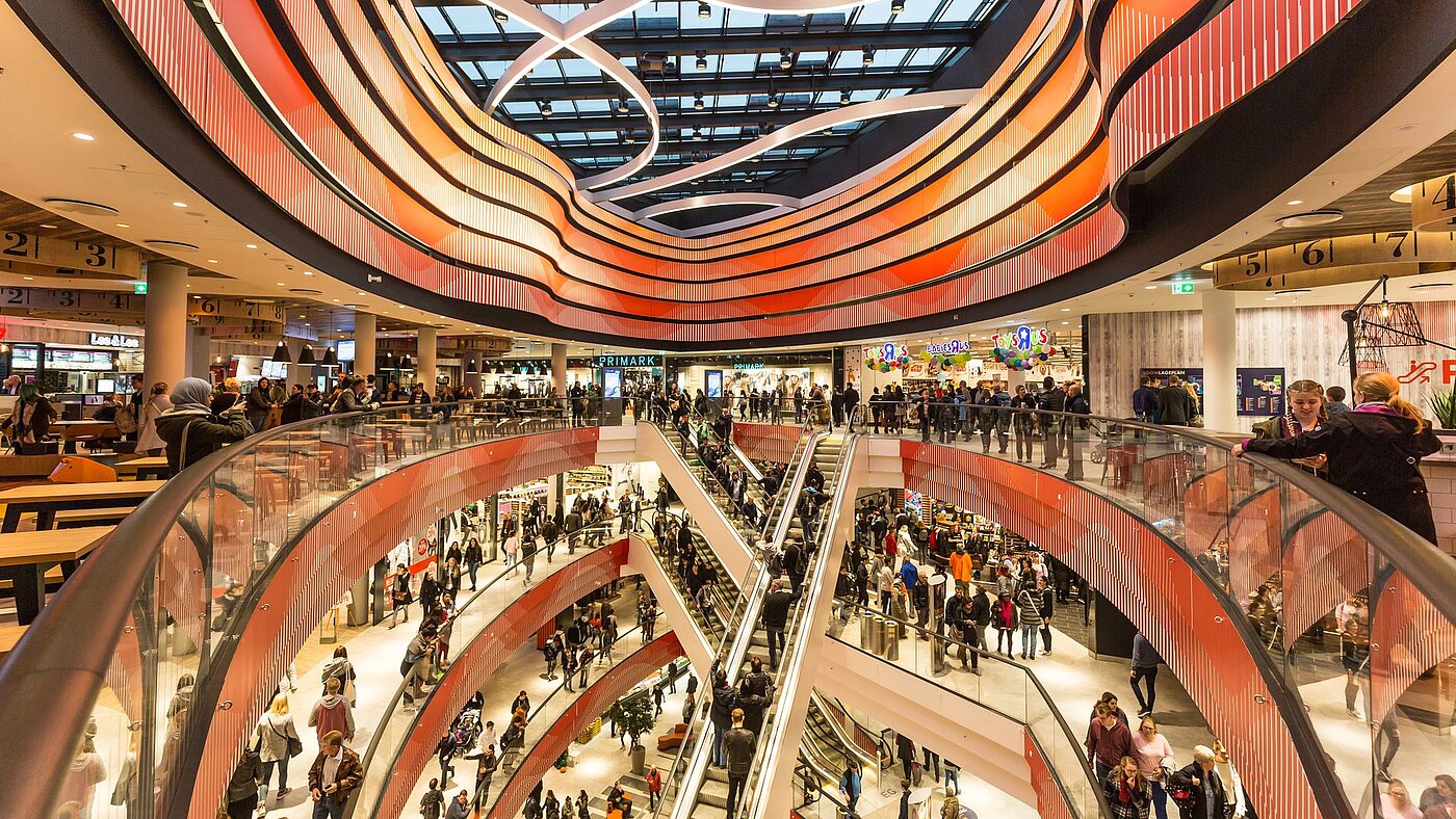 Im Inneren eines Shopping-Centers mit imposanter roter Deckenbeleuchtung und vielen Besucherinnen und Besuchern in den Kaufhaus-Gängen